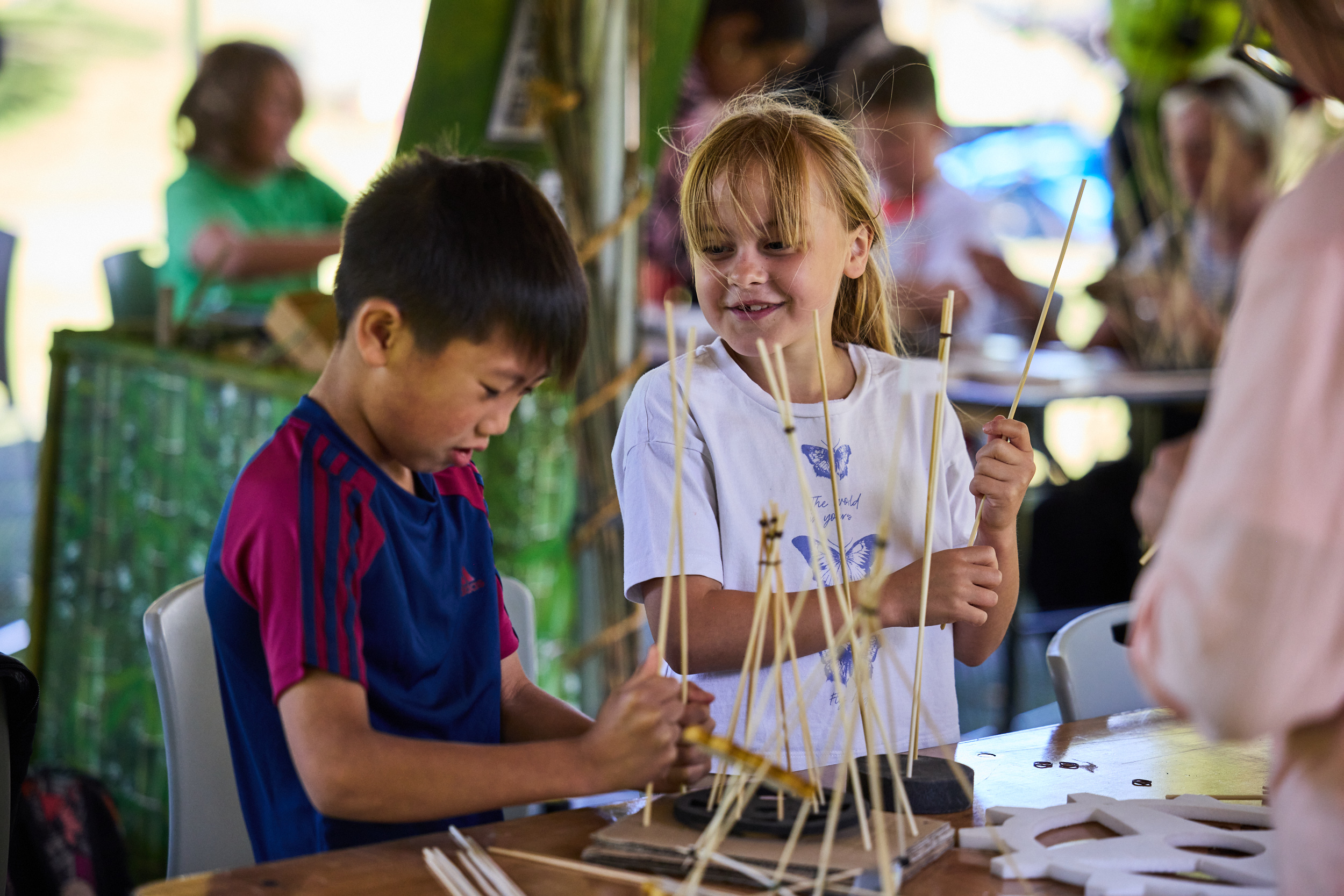 Two children make bamboo crafts in a tent