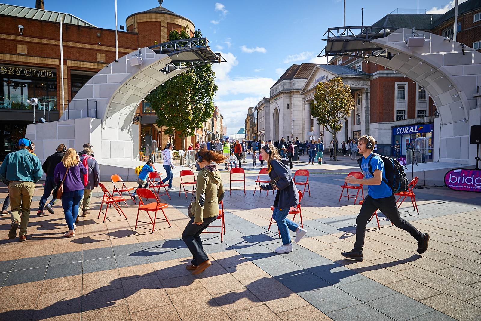 Under the broken bridge, a group of 15 people are wearing headphones and running around in a circle.