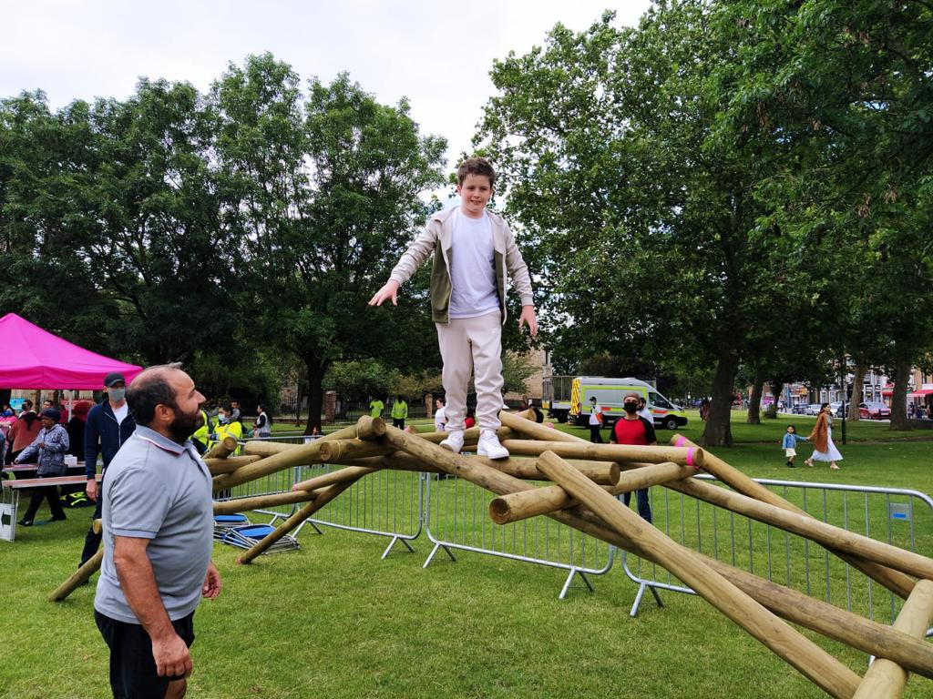A boy aged around 10 years balances his way across the self-supporting bridge, with an onlooker ready to help should he lose his balance